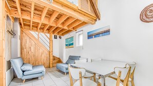 A room with a wooden ceiling, a white table with four chairs, a blue sofa, and a staircase.