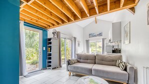 Un salon moderne avec un canapé gris, des poutres en bois au plafond et un coin repas comprenant une table et des chaises.