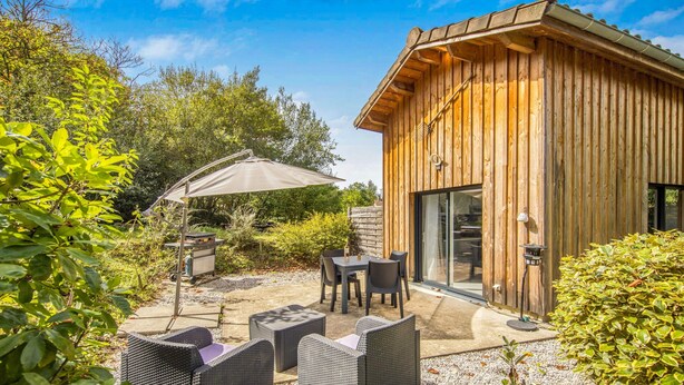Une cabane en bois dotée d’une terrasse, de mobilier d’extérieur et d’un grand parasol.