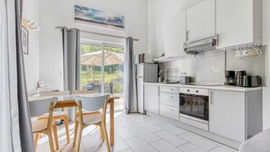 Une cuisine moderne avec des meubles blancs, un coin repas avec deux chaises et une grande fenêtre agrémentée de rideaux.