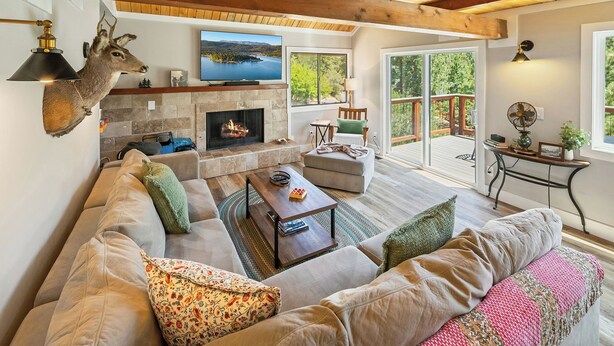 A cozy living room with a stone fireplace, a mounted deer head, and a large TV.