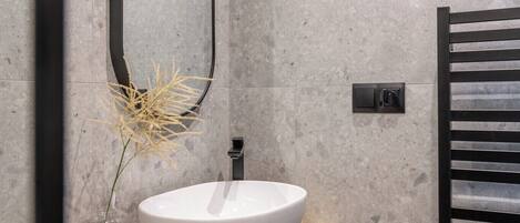 A modern bathroom with a freestanding wooden vanity, a white sink, a mirror, and a towel rack.