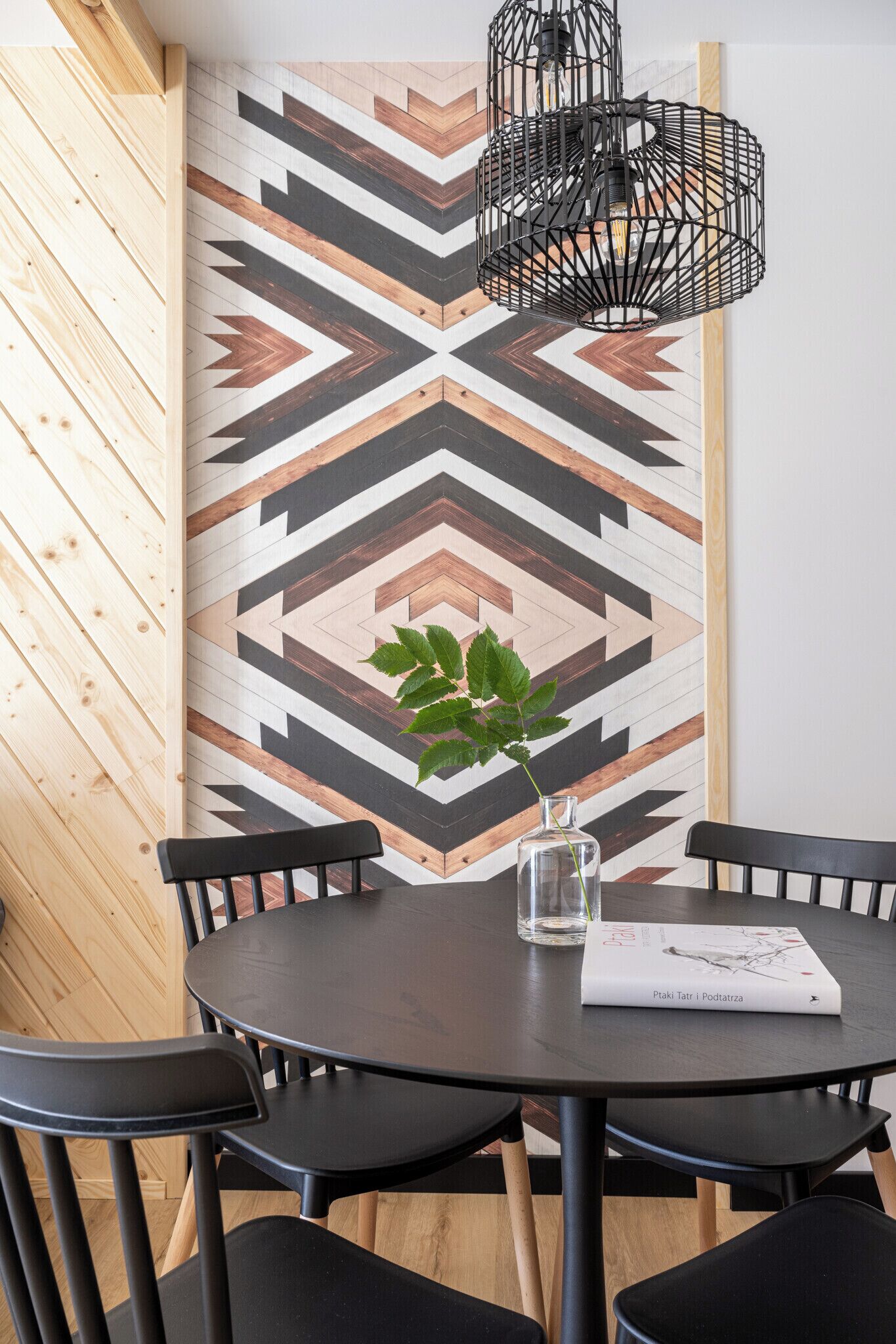 A dining area with a round table, black chairs, a geometric patterned wall, and a hanging black light fixture.