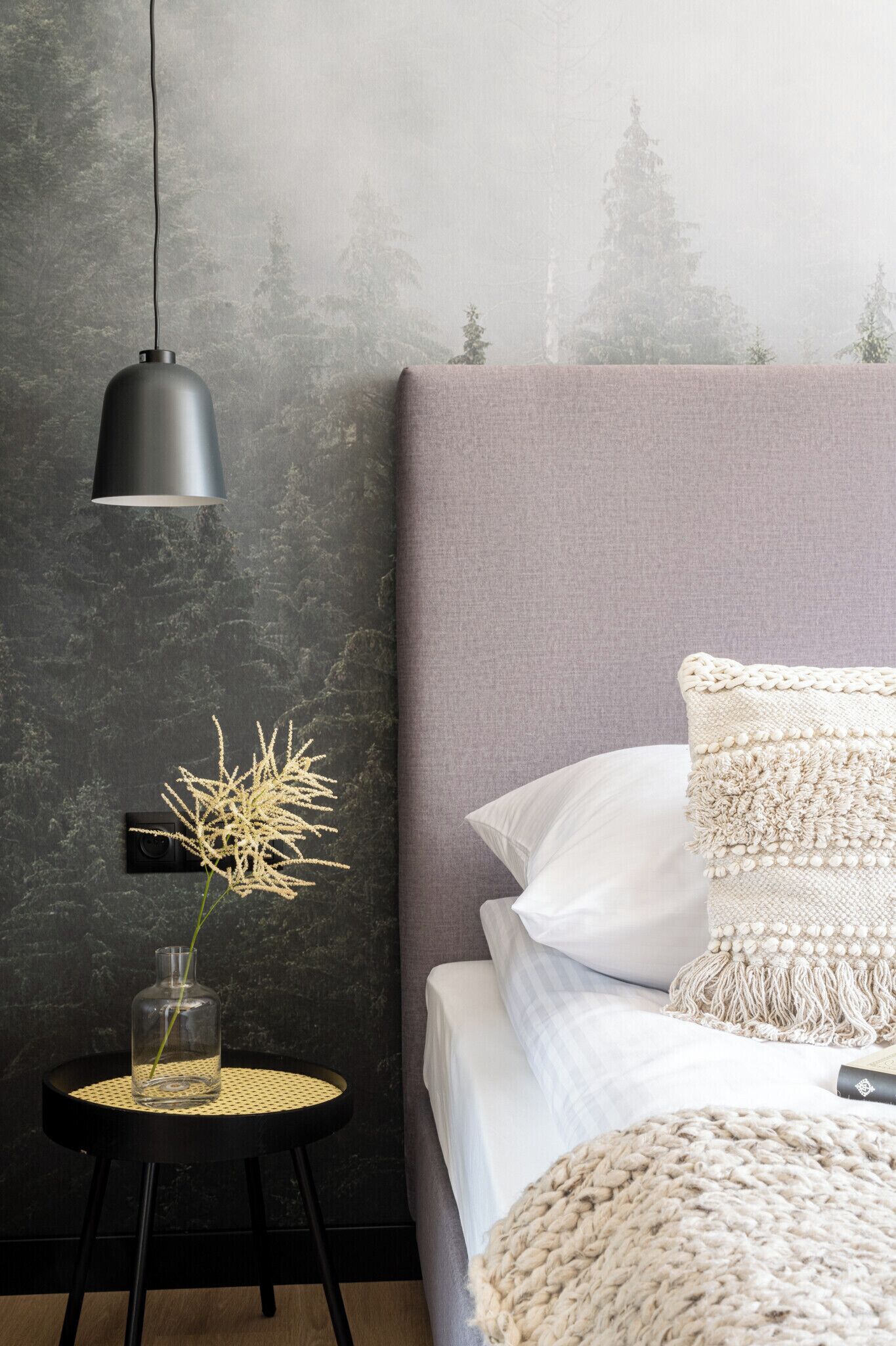 Una camera da letto con un letto, un tavolino rotondo con un vaso, una lampada a parete e una parete con una superficie strutturata.