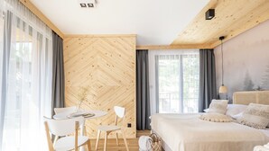 Une chambre moderne avec un mur en bois disposé en motif chevron, une table de salle à manger ronde avec des chaises, un lit avec une tête de lit blanche et une grande fenêtre avec des rideaux.