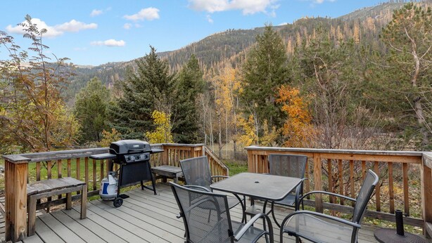 A deck with outdoor furniture, a grill, and a view of a forested hillside.