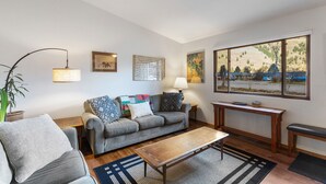 A living room with a sofa, armchairs, a coffee table, and a large window with a view of a residential area.