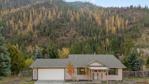 A single-story house with a garage, surrounded by a forested hillside.