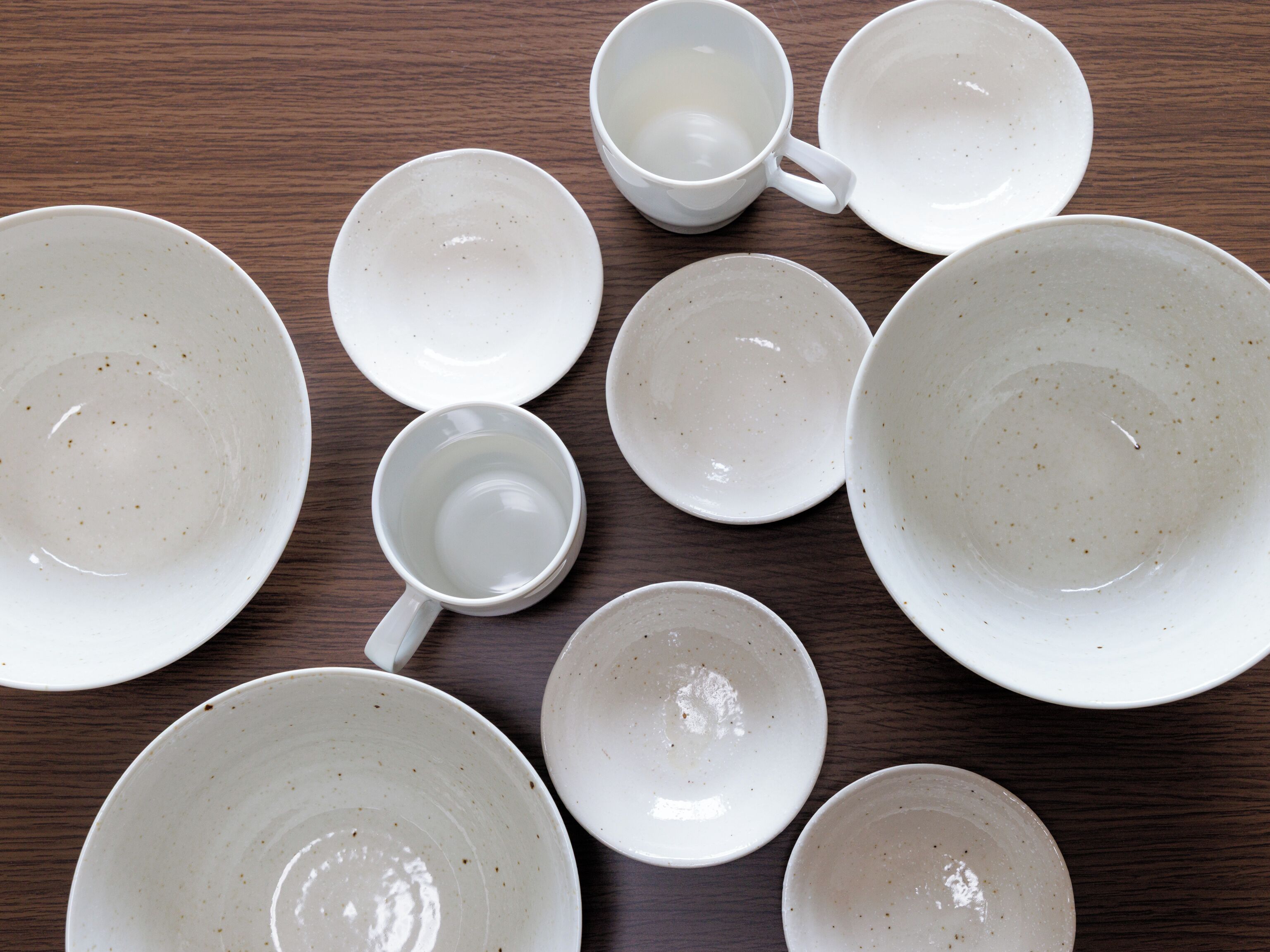 A collection of white ceramic plates and cups arranged on a wooden table.