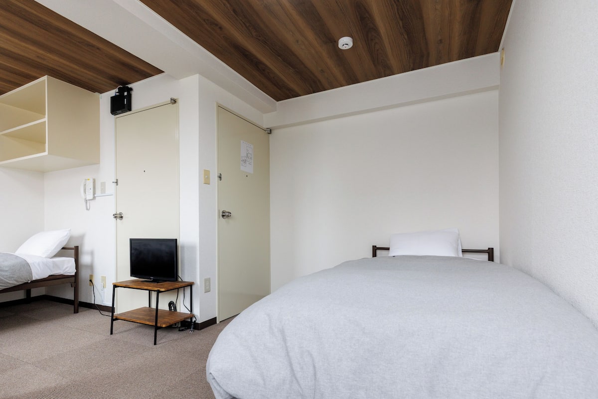 Une chambre d’hôtel avec un lit, un bureau équipé d’un ordinateur, une chaise et un téléphone fixé au mur.