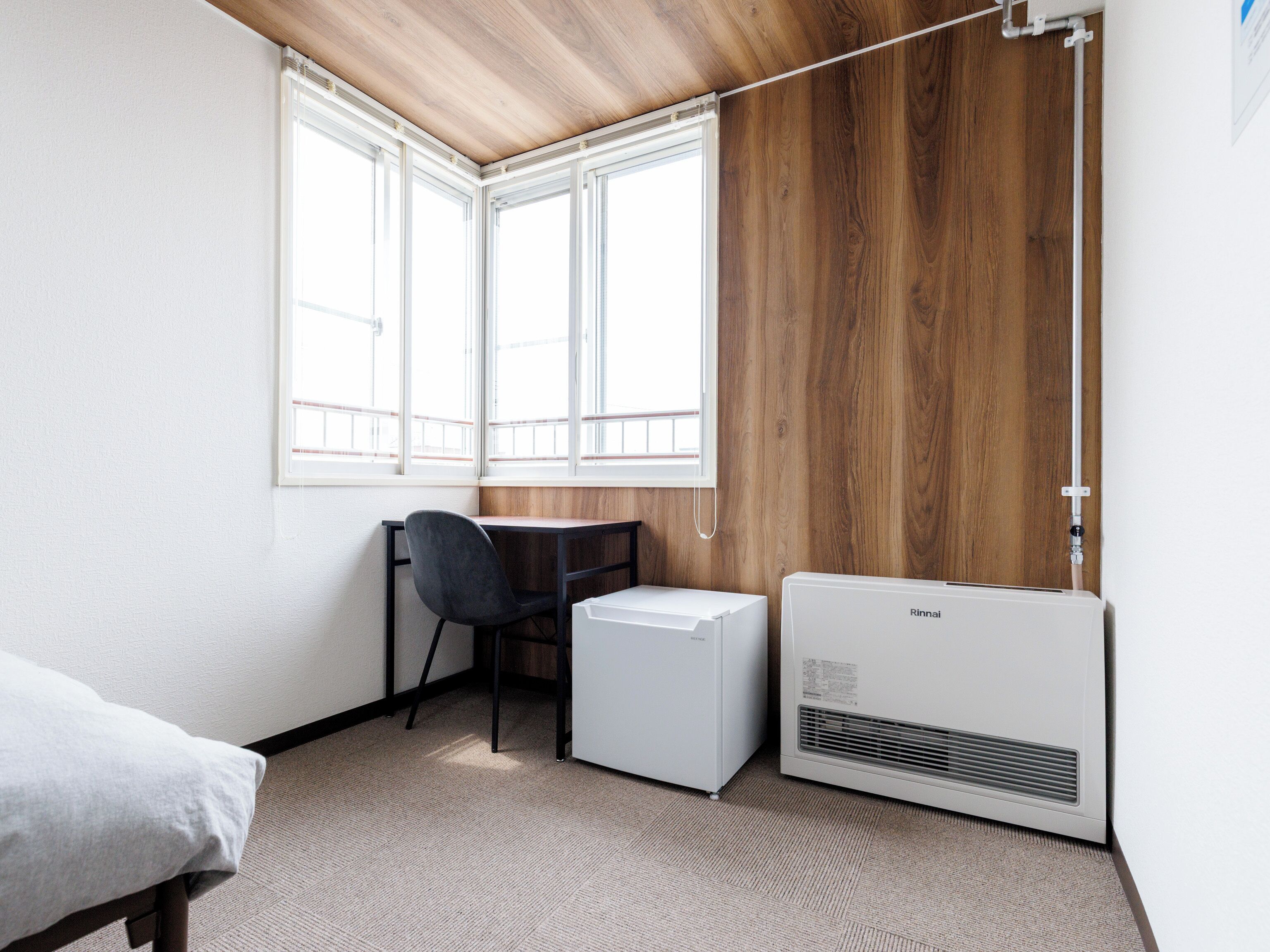 Ein Zimmer mit Schreibtisch in der Ecke, einem Sessel, einem Bett und einer weißen Klimaanlage.