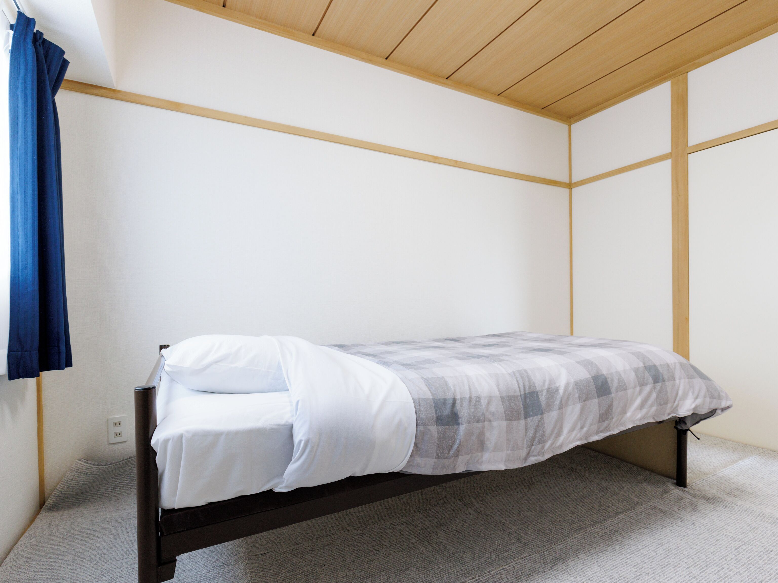 A small, single-bed room with a wooden ceiling and white walls.