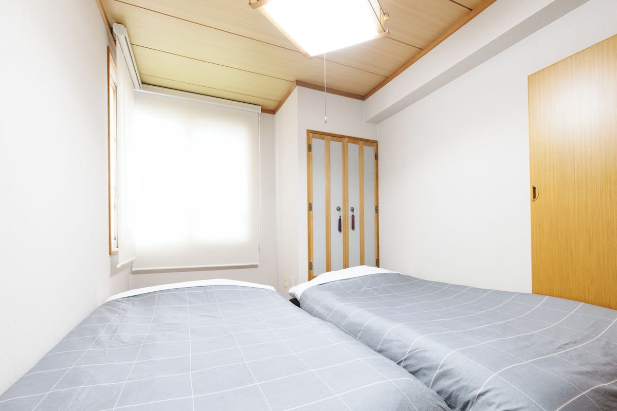 Une chambre avec deux lits simples, une armoire en bois, une fenêtre avec des stores et un plafond en pente doté d’un puits de lumière.