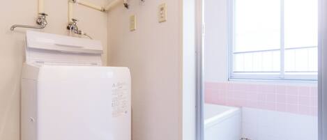 Een badkamer met een witte wasmachine, een raam en roze betegelde muren, en een betegelde vloer.