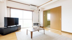 A modern living room with a flat-screen TV, a coffee table, and a large window. - Tabist JKN Twin Hotel (Asahikawa)