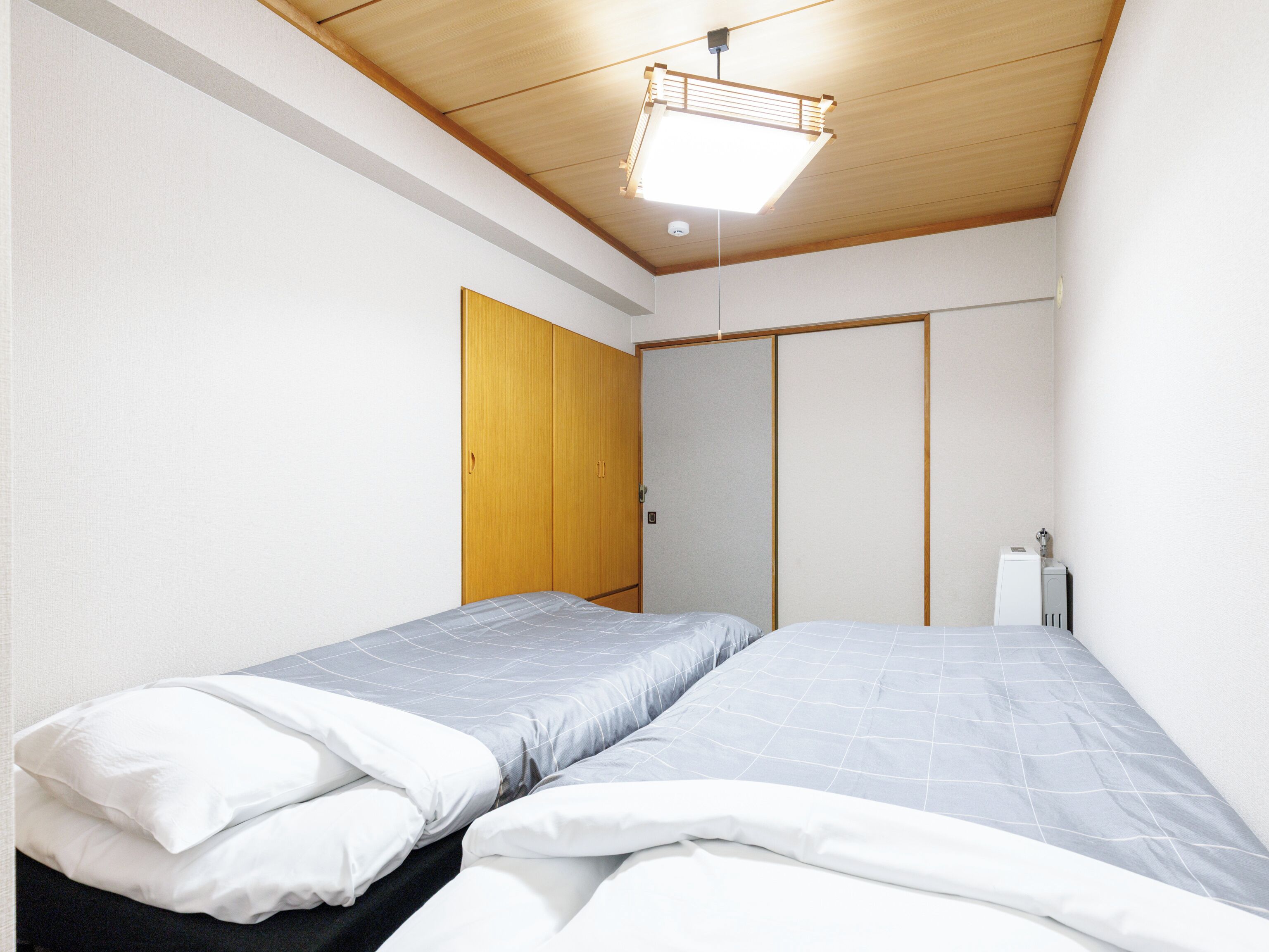 Un dormitorio con dos camas, un armario de madera y una lámpara en el techo.