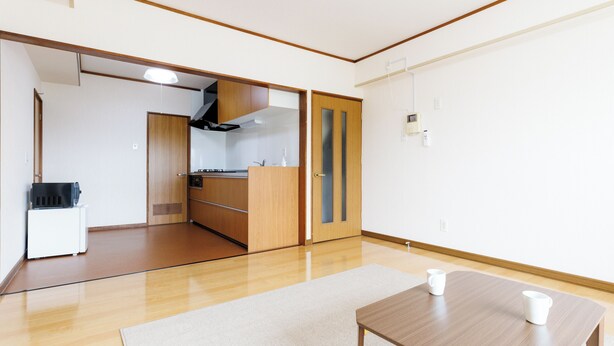 A modern, minimalist room with a wooden floor, a white rug, a wooden table with two white cups, and a kitchen area with wooden cabinets and a stove. - Tabist JKN Twin Hotel (Asahikawa)