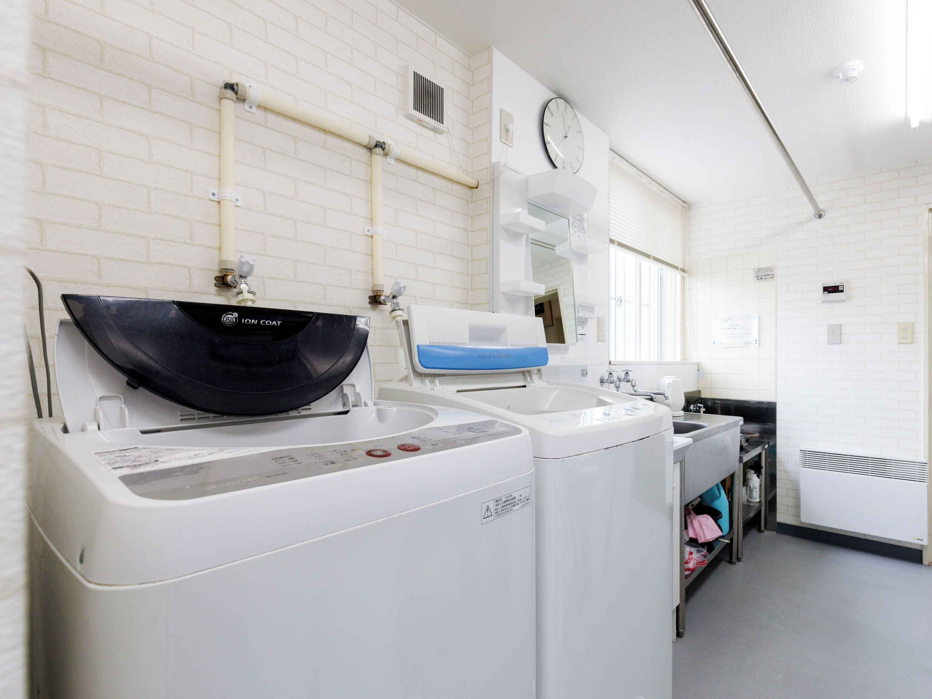 A modern laundry facility with two washing machines, a sink, and a mirror.