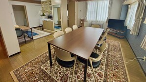 A conference room with a long table, chairs, a television, and a kitchen area in the background. - Tabist JKN Twin Hotel (Asahikawa)