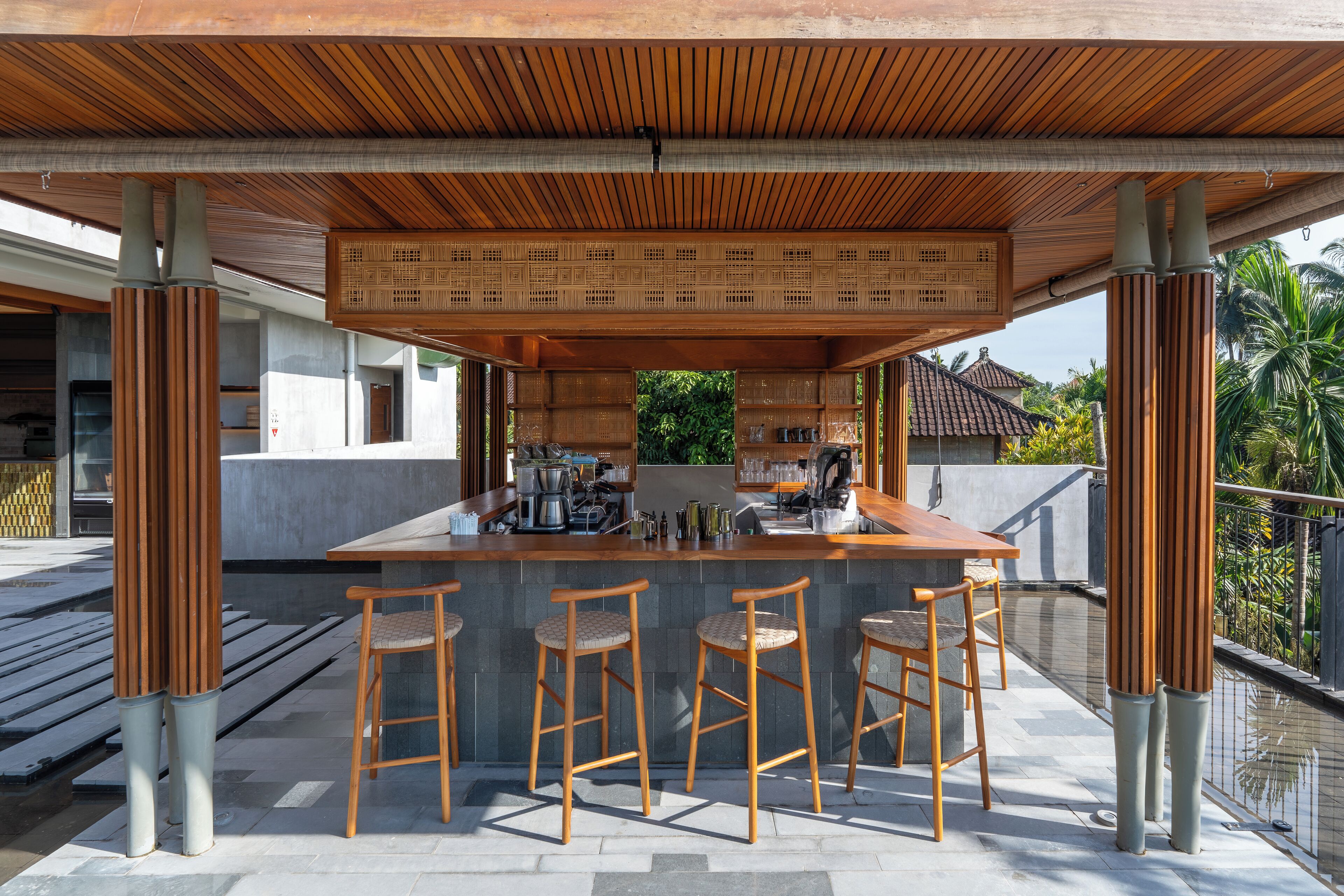 Een buitengebied met een bar, voorzien van een houten plafond, een stenen aanrecht en vier houten barstoelen.