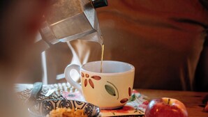 A person pouring coffee into a cup with a floral design, placed on a coaster with an apple and a bowl of nuts. - Agriturismo Le Noci (Tarzo)