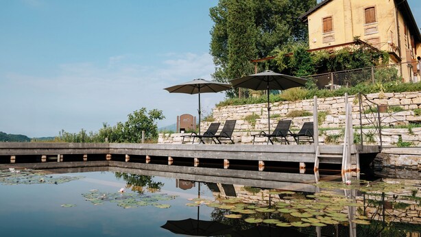 A pool area with lounge chairs and umbrellas, a stone wall, and a building with a yellow facade. - Agriturismo Le Noci (Tarzo)