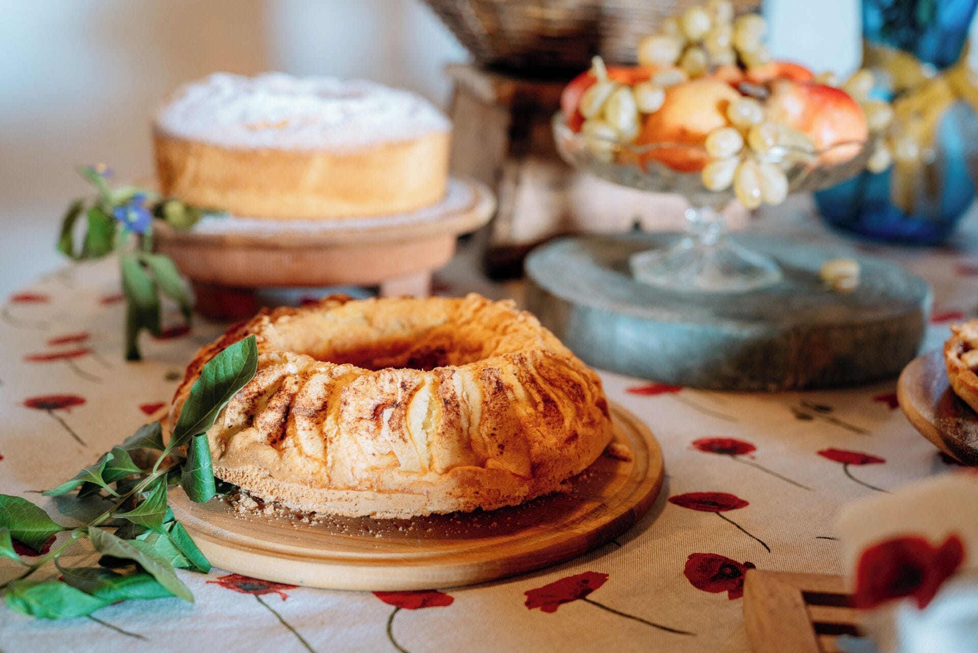 A table with a bundt cake, a fruit bowl, and a decorative item.