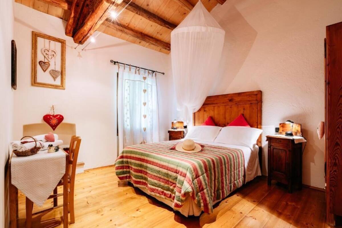 Um quarto aconchegante com teto de madeira, cama com colcha listrada, mesa de cabeceira com abajur e uma cadeira com toalha de mesa.
