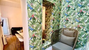 A room with a tropical wallpaper, a grey sofa, and a dining area with white chairs. - Exclusive suite in the historic center of Catania, private entrance (Catania)
