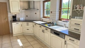 A modern kitchen with white cabinetry, a stainless steel range hood, a built-in dishwasher, and a window providing a view of the outdoors. - Villa Marie Frances (DURBUY)
