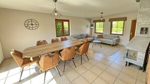 A spacious living area with a wooden dining table, multiple chairs, a sofa, and a fireplace. - Villa Marie Frances (DURBUY)