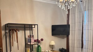 A hotel room with a bed, a desk, a chair, a TV, a wardrobe, and a chandelier. - A village that preserves memory. A place to inhabit, not just to visit. (Cosenza)