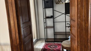A room with a wooden door, a black metal shelving unit, a patterned rug, and a chair. - A village that preserves memory. A place to inhabit, not just to visit. (Cosenza)
