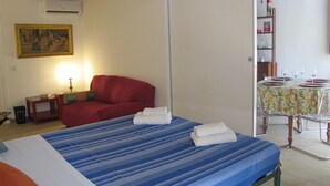 Una habitación con una cama, un sofá rojo, una mesa de comedor para cuatro personas y un cuadro en la pared.