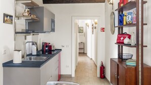 Una cocina moderna con un lavamanos, estufa y diversos utensilios de cocina. Se ve un pasillo que conduce a otra habitación con una puerta y un extintor.