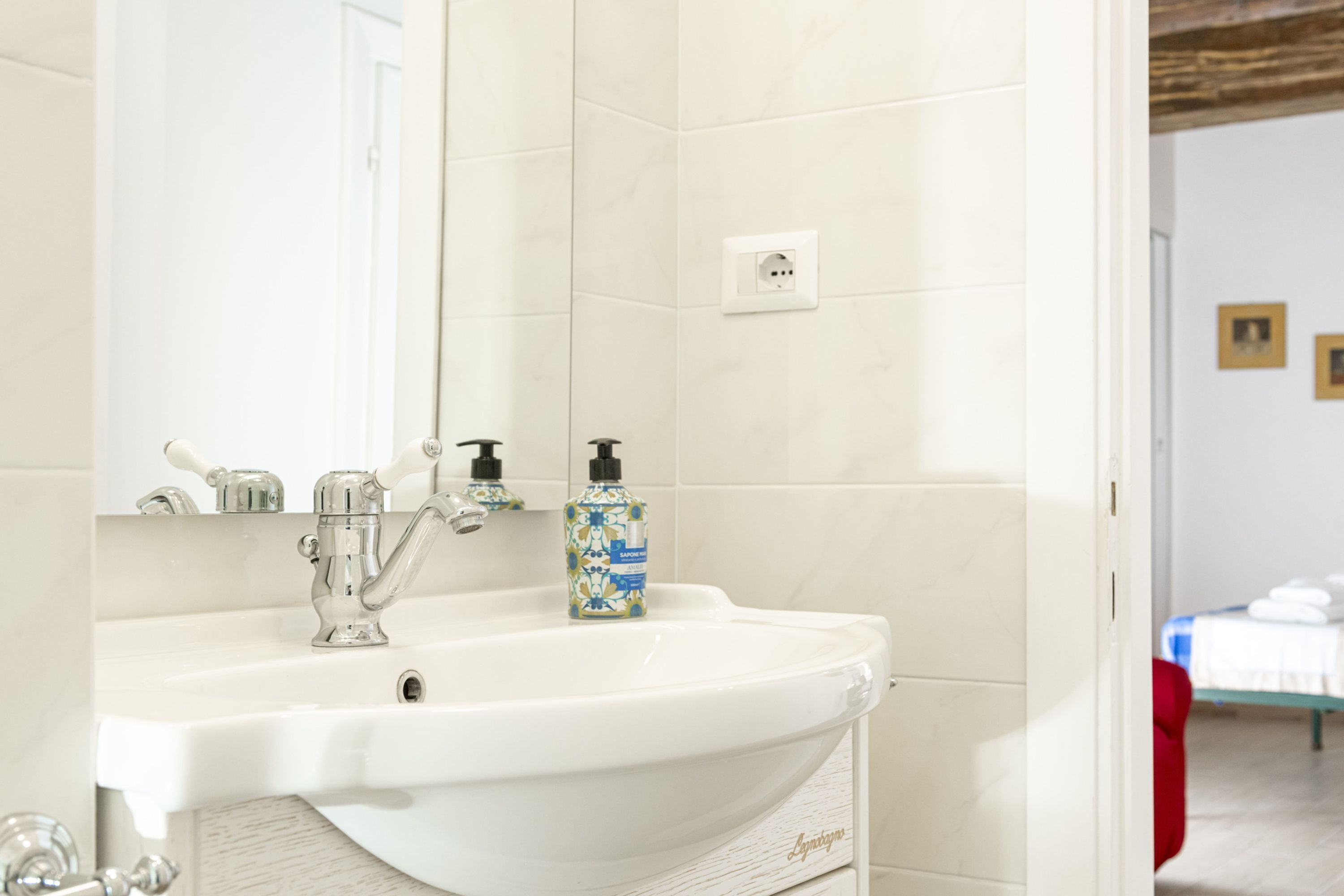 A bathroom with a white sink, a mirror, and a bottle of hand soap.