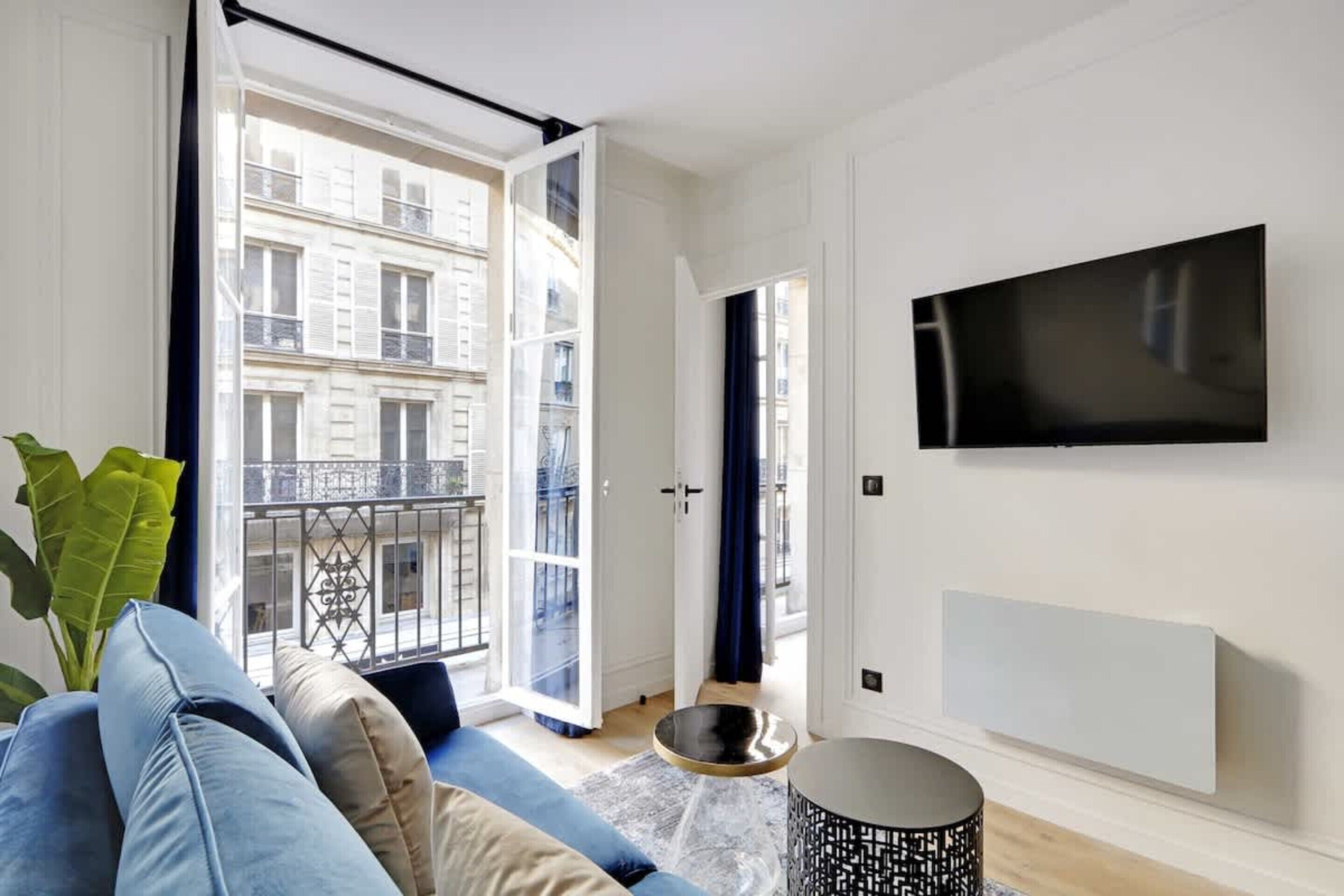 Una sala de estar moderna con un televisor grande, un sofá, una mesa de centro y un balcón con vistas a edificios.