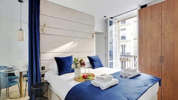A modern hotel room with a large bed, a dining area, and a view of the city.