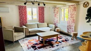 Een gezellige woonkamer met een bank, fauteuil en salontafel. Gordijnen, een radiator en een plant zijn aanwezig.