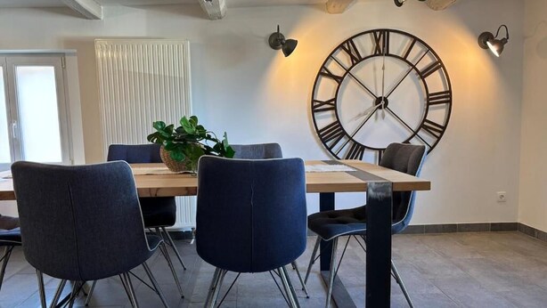 Een eetruimte met een houten tafel, vier stoelen en een grote wandklok.