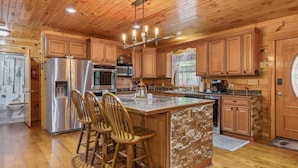 A spacious kitchen with wooden cabinets, a large island with bar stools, stainless steel appliances, and a window overlooking the outdoors.