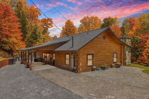 A rustic wooden building with a covered porch, a stone chimney, and a gravel driveway. - Spacious Dog-Friendly 3BR Sevierville Cabin w/ Air Hockey, Fire Pit & EV Charger (Sevierville)