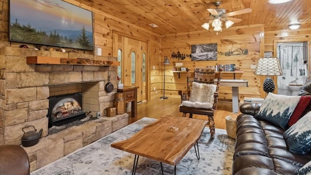 A cozy log cabin interior with a stone fireplace, leather sofa, and wooden furniture.