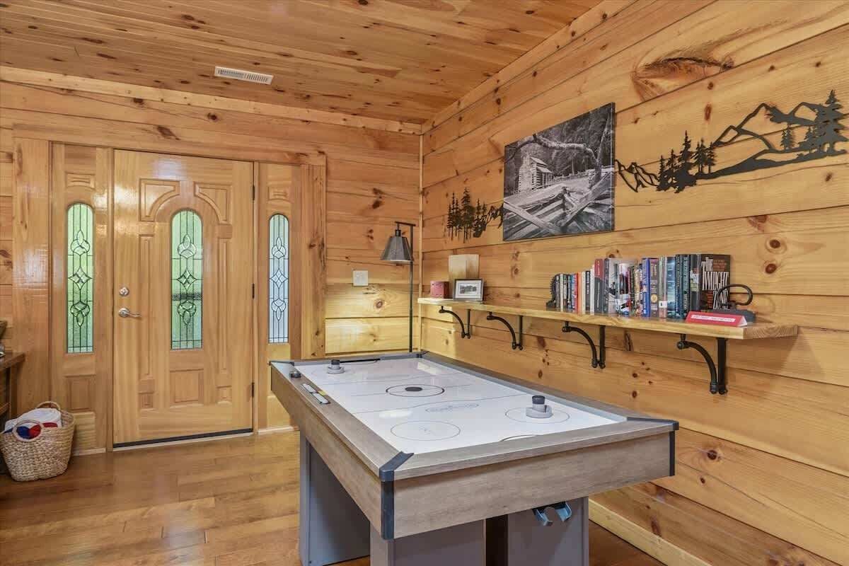 A wooden interior with a pool table, wooden doors with glass panels, and a shelf with books.