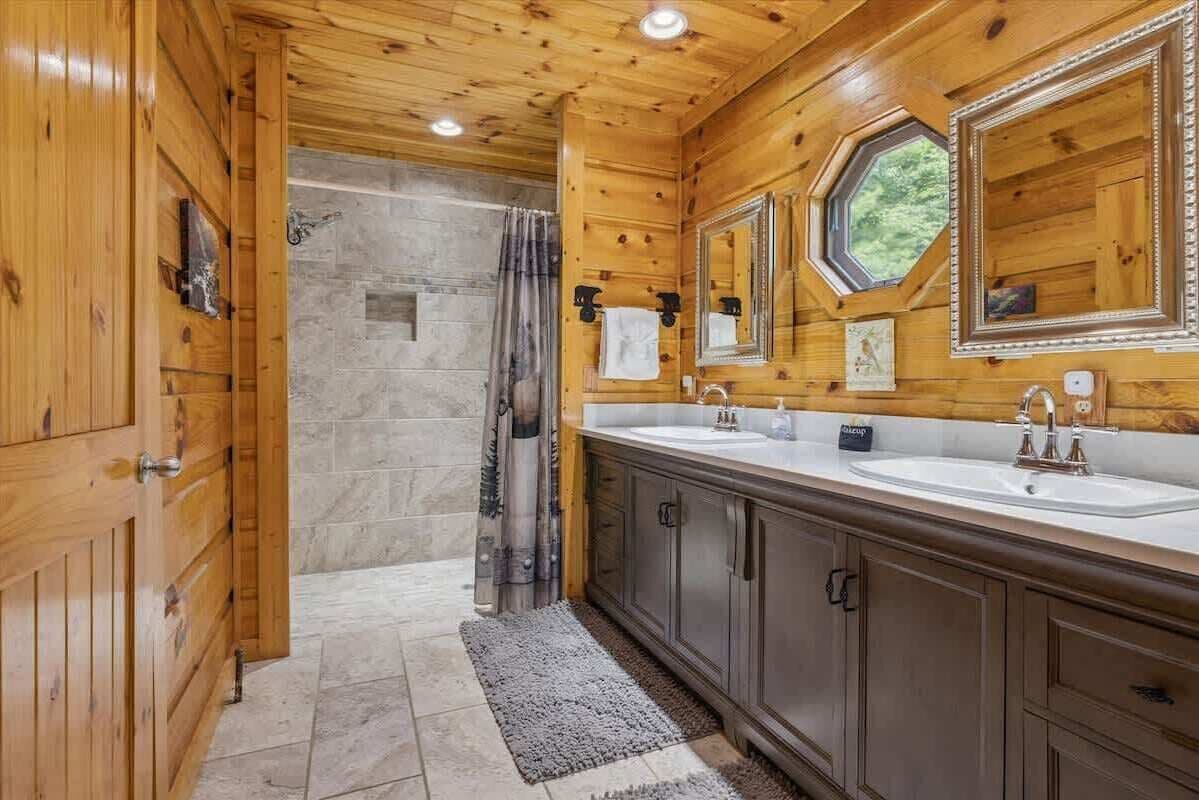 Ein Badezimmer einer Holzhütte mit einer Steindusche, einem großen Spiegel und einem Fenster.