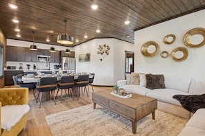 Eine moderne Küche mit Holzschränken, ein Essbereich mit Tisch und Stühlen sowie ein Wohnzimmer mit Sofa und Couchtisch.