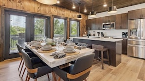 Une cuisine moderne avec un lambris en bois, des appareils en acier inoxydable et une grande table à manger pouvant accueillir six personnes.