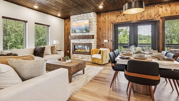 Un salon moderne avec une cheminée en pierre, un plafond en bois et de grandes fenêtres.