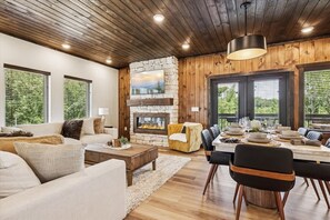 Ein modernes Wohnzimmer mit Kamin aus Stein, Holzboden und großen Fenstern.