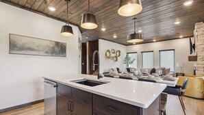 Une cuisine moderne dotée d’un îlot central, de luminaires suspendus et d’un coin repas avec une chaise jaune.